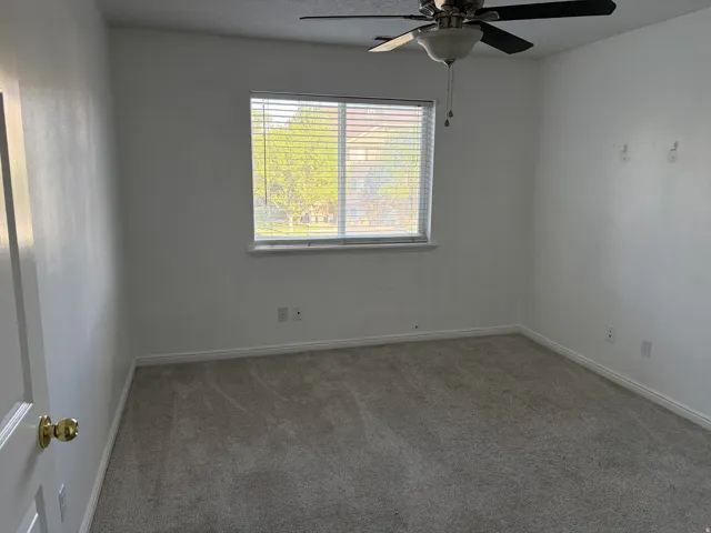 Window with horizontal blinds, overhead ceiling fan with light fixture, light-toned wall-to-wall carpeting, and white baseboards