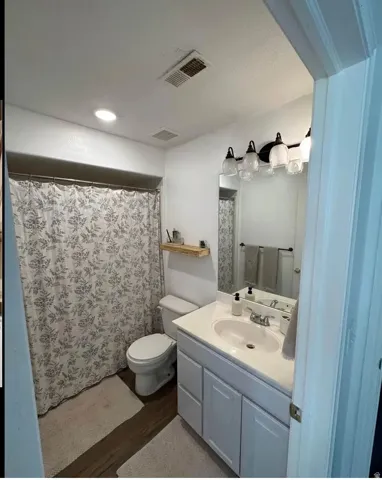 Bathroom featuring a white vanity with an integrated sink, dark wood-finish flooring, a contemporary light fixture, and a floating wood shelf