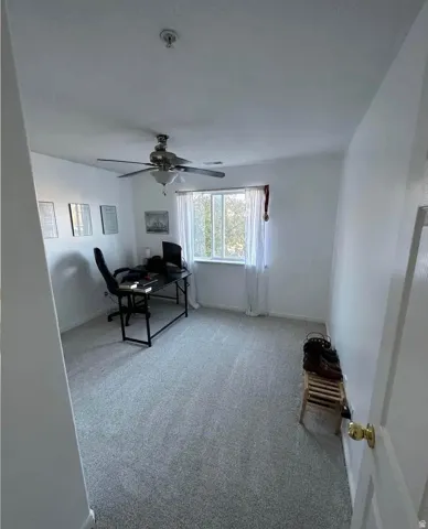 Spacious room featuring light gray carpeting, neutral wall finishes, and a ceiling fan with integrated lighting