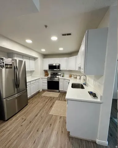 Modern kitchen featuring white cabinetry, light countertops, wood-finish flooring, stainless steel appliances, and recessed lighting