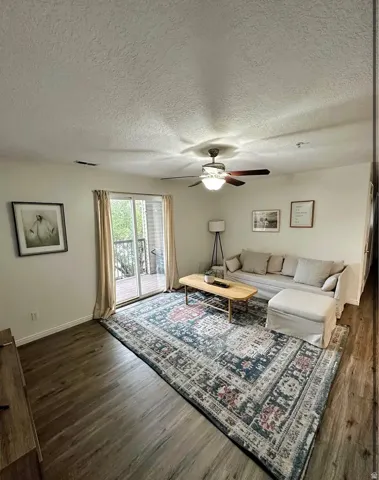 Living space featuring wood-finish flooring, a ceiling fan with light fixture, and a sliding glass door providing exterior access