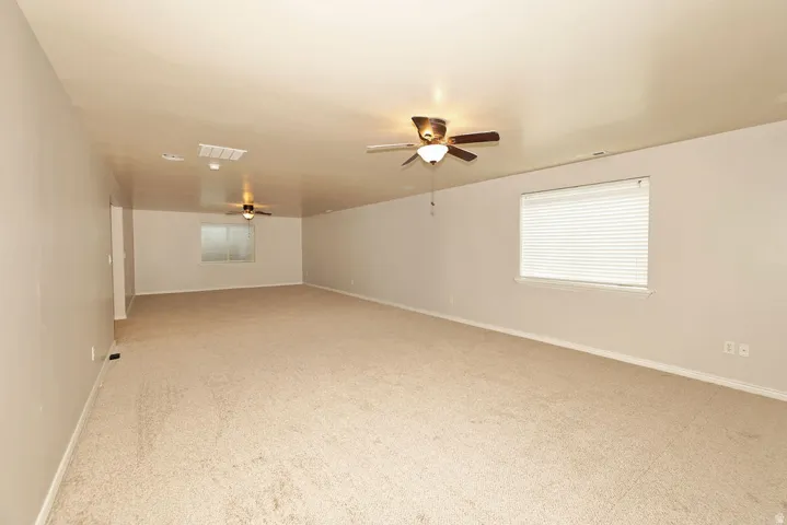 Spacious bonus room featuring neutral carpet flooring, recessed ceiling lighting, ceiling fan with integrated light fixture, and large window with plantation shutters providing natural illumination