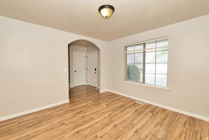 Bright and spacious room showcasing gleaming wood-finish flooring, clean white walls, and abundant natural light from a large multi-pane window
