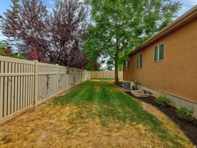 Spacious backyard featuring a mature landscaped setting with established trees, manicured lawn, and vinyl privacy fencing