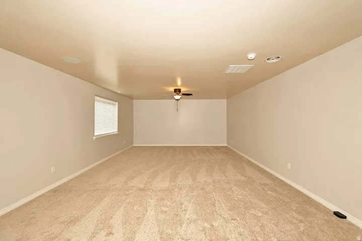 Spacious room featuring neutral carpeting, a ceiling fan, a window with horizontal blinds, and recessed ceiling speakers
