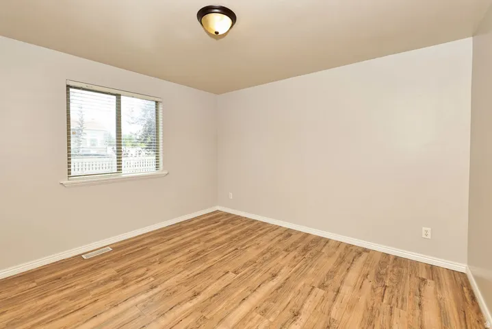 Bright corner bedroom with wood-finish flooring, neutral walls, and abundant natural light from dual windows