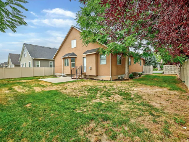 Expansive backyard featuring a concrete patio, mature trees providing natural shade, and a full perimeter fence