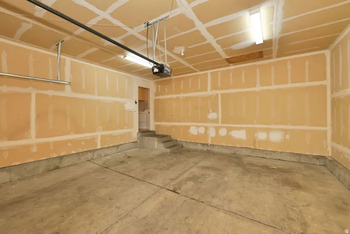 Spacious garage interior featuring concrete flooring, wood-framed wall construction, exposed ceiling joists with integrated lighting, and overhead garage door mechanism