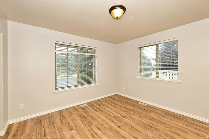 Room featuring wood-finish flooring, two windows with blinds, a ceiling-mounted light fixture, and neutral painted walls