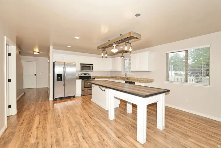 Open-concept kitchen with wood-finish flooring, white cabinetry, stainless steel appliances, and granite countertops
