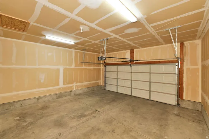 Garage featuring a concrete floor, exposed drywall, overhead fluorescent lighting, and an automatic garage door opener