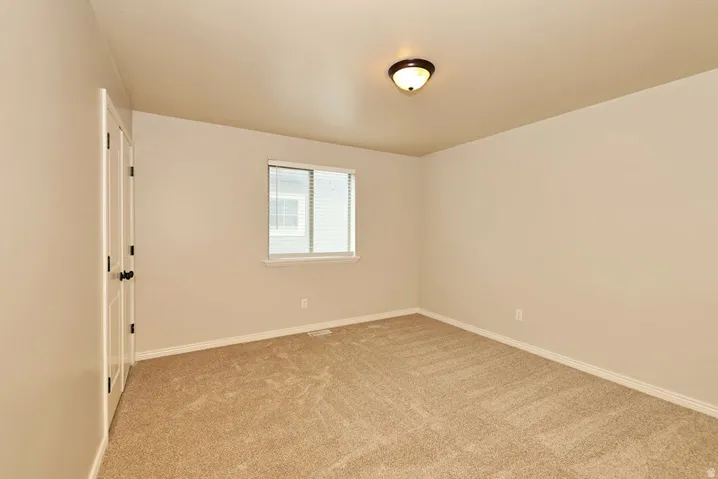 Bright and spacious bedroom featuring neutral wall finishes, carpeted flooring, a large double-hung window with natural light, ceiling-mounted fixture, and a white six-panel entry door