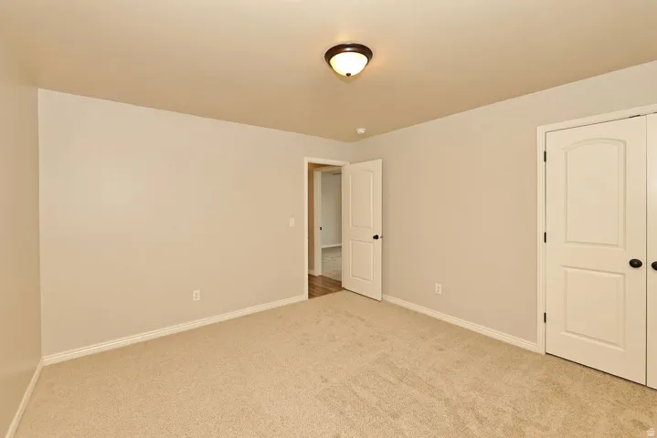 Spacious bedroom featuring neutral carpet flooring, soft ambient lighting from ceiling fixture, and dual closet doors providing ample storage