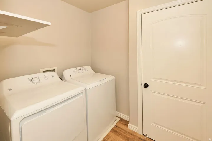 Dedicated laundry room featuring side-by-side washer and dryer with intuitive control panels, neutral cabinetry, recessed lighting, wood-finish flooring, and a six-panel interior door for privacy and separation from living spaces