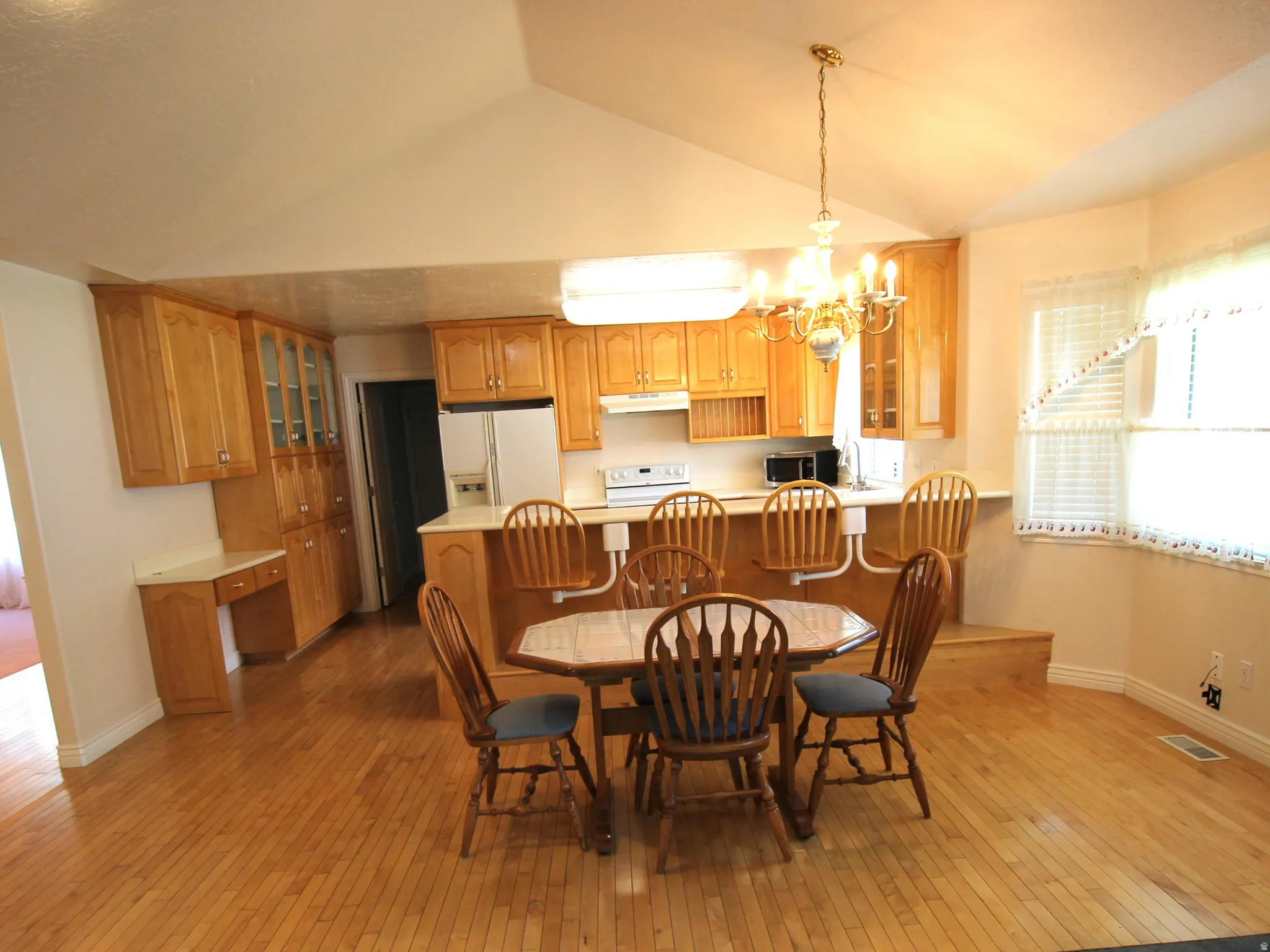Hardwood flooring, vaulted ceiling, built-in kitchen cabinetry, kitchen counter seating, and bay window