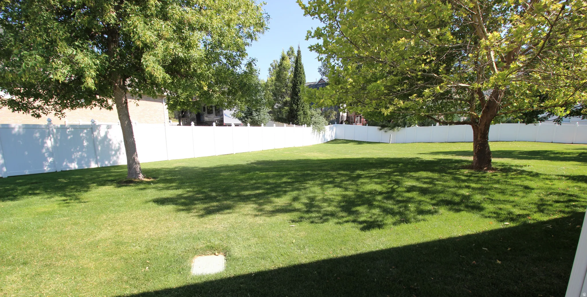Expansive grassy yard featuring mature trees, a full perimeter vinyl fence, and ample open space