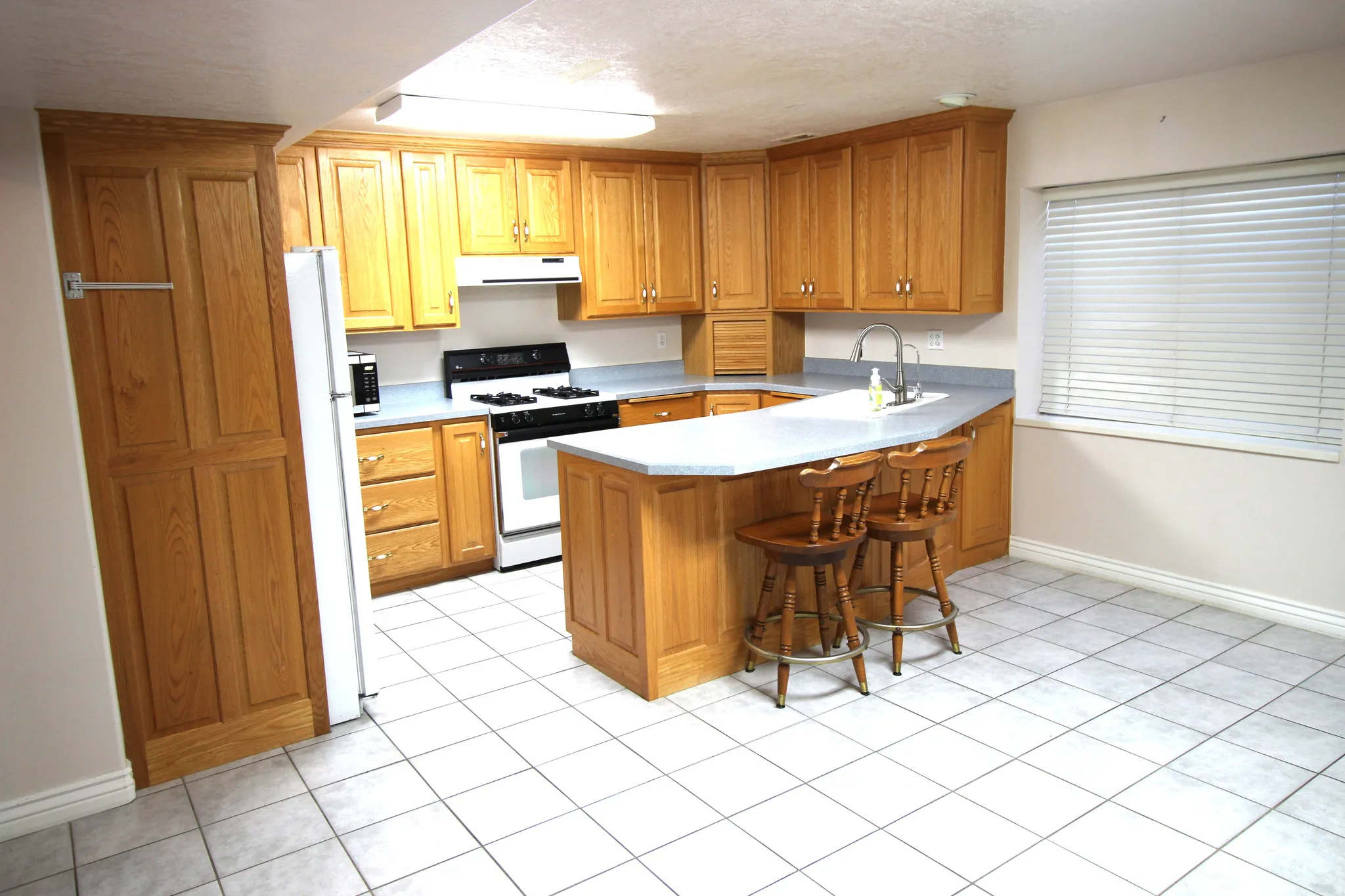 Kitchen featuring wood cabinetry, white tile flooring, L-shaped counter seating, and a built-in pantry