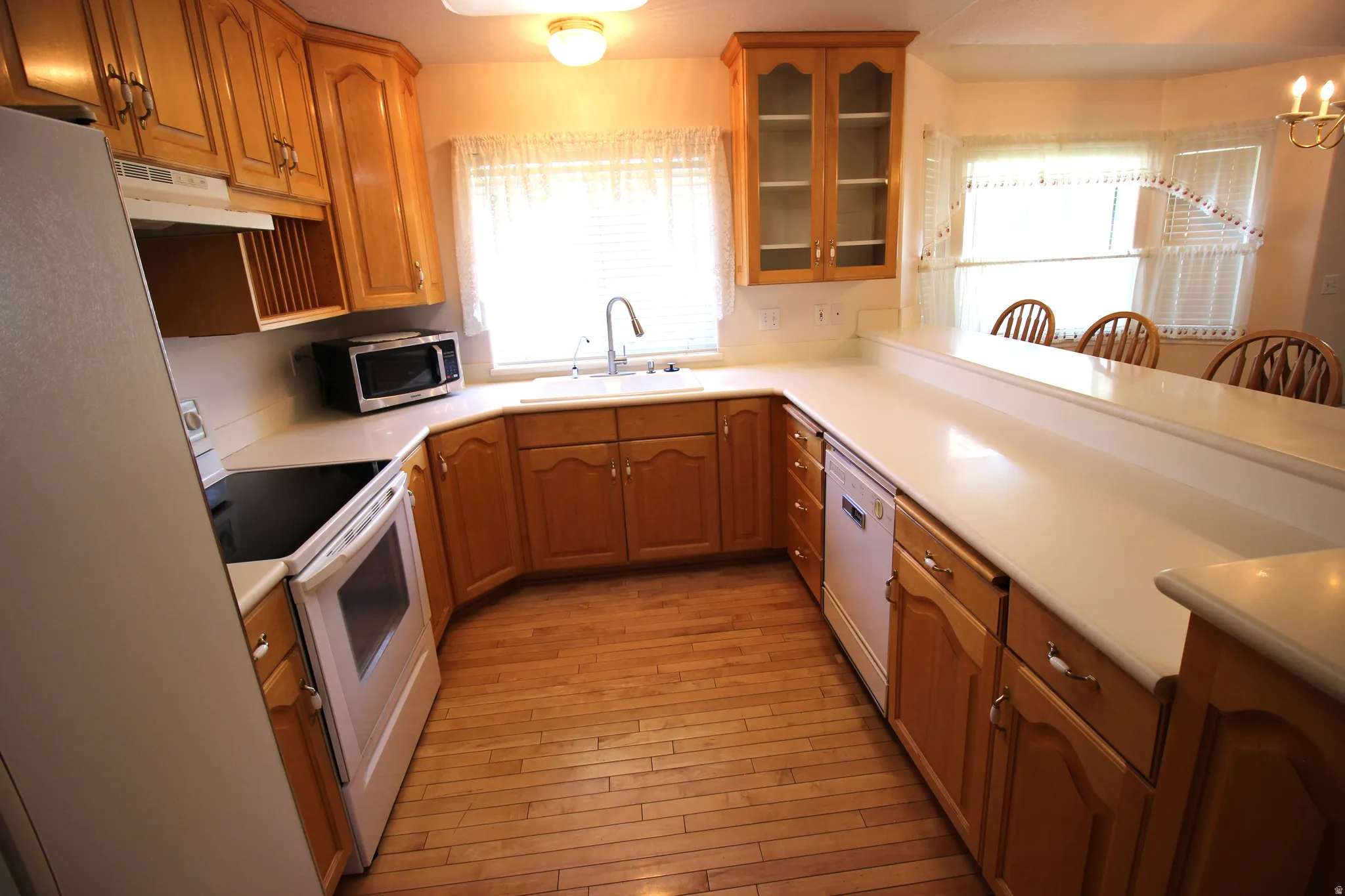 U-shaped kitchen featuring wood-finish cabinetry, light-toned countertops, a built-in range, and a breakfast bar