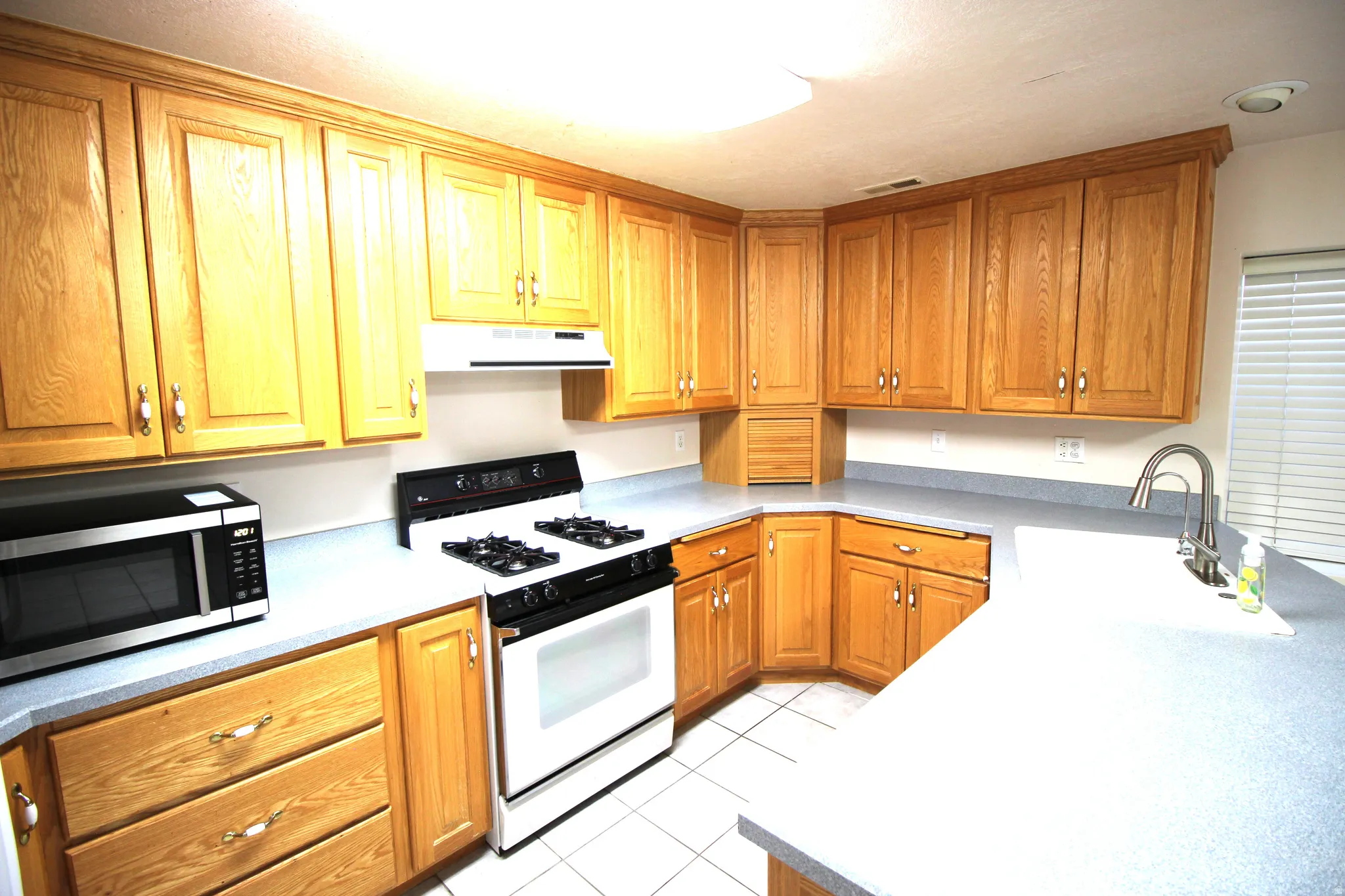 Expansive kitchen featuring light wood cabinetry, a white gas range with a range hood, and a dual-basin stainless steel sink with a gooseneck faucet