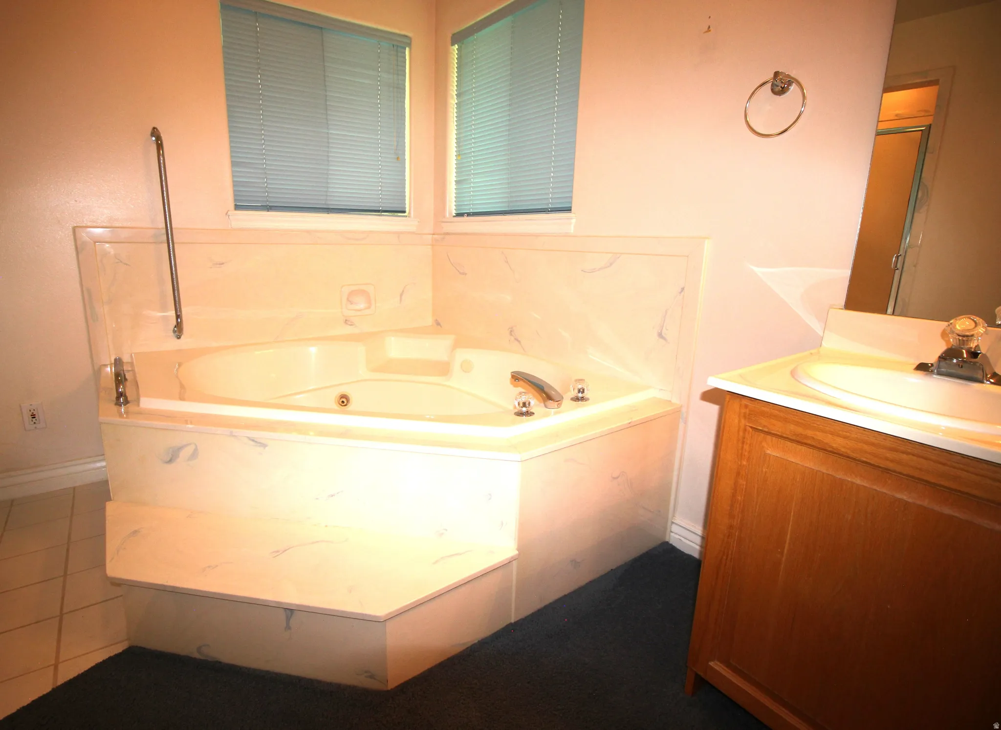 Corner jetted bathtub with a grab bar, featuring a tile surround and steps