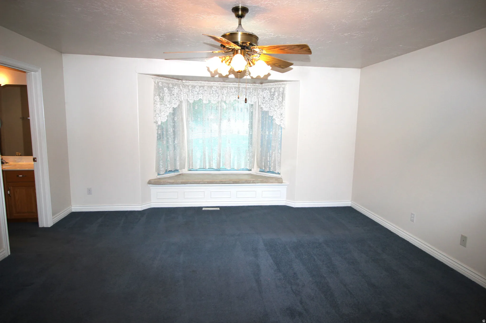Spacious Master Bedroom with blue carpeting, a bay window with integrated window seat, and a ceiling fan with integrated lighting