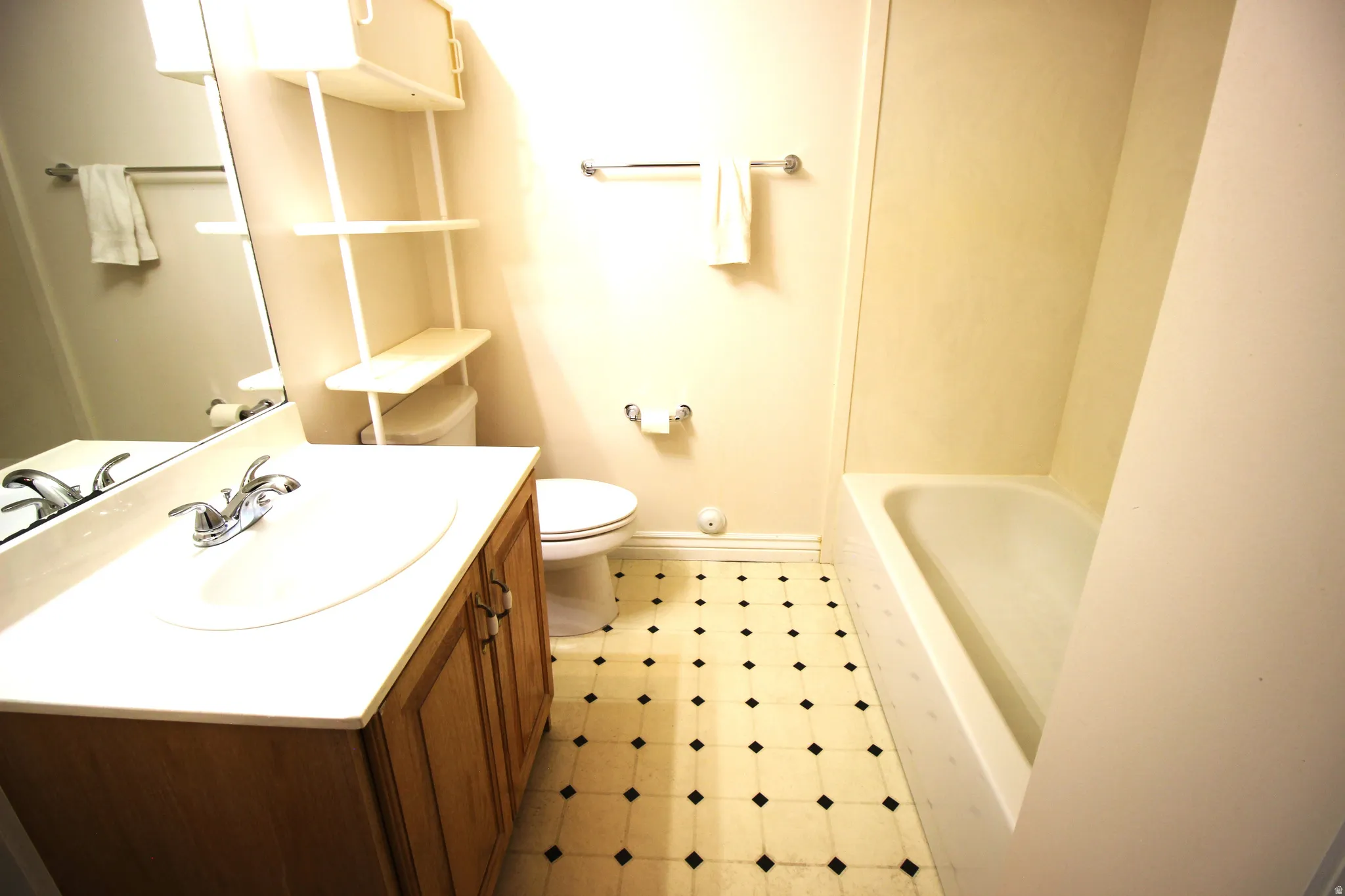 Bathroom featuring a vanity with a laminate countertop, chrome fixtures, built-in shelving, a toilet, and a tub with tiled surround