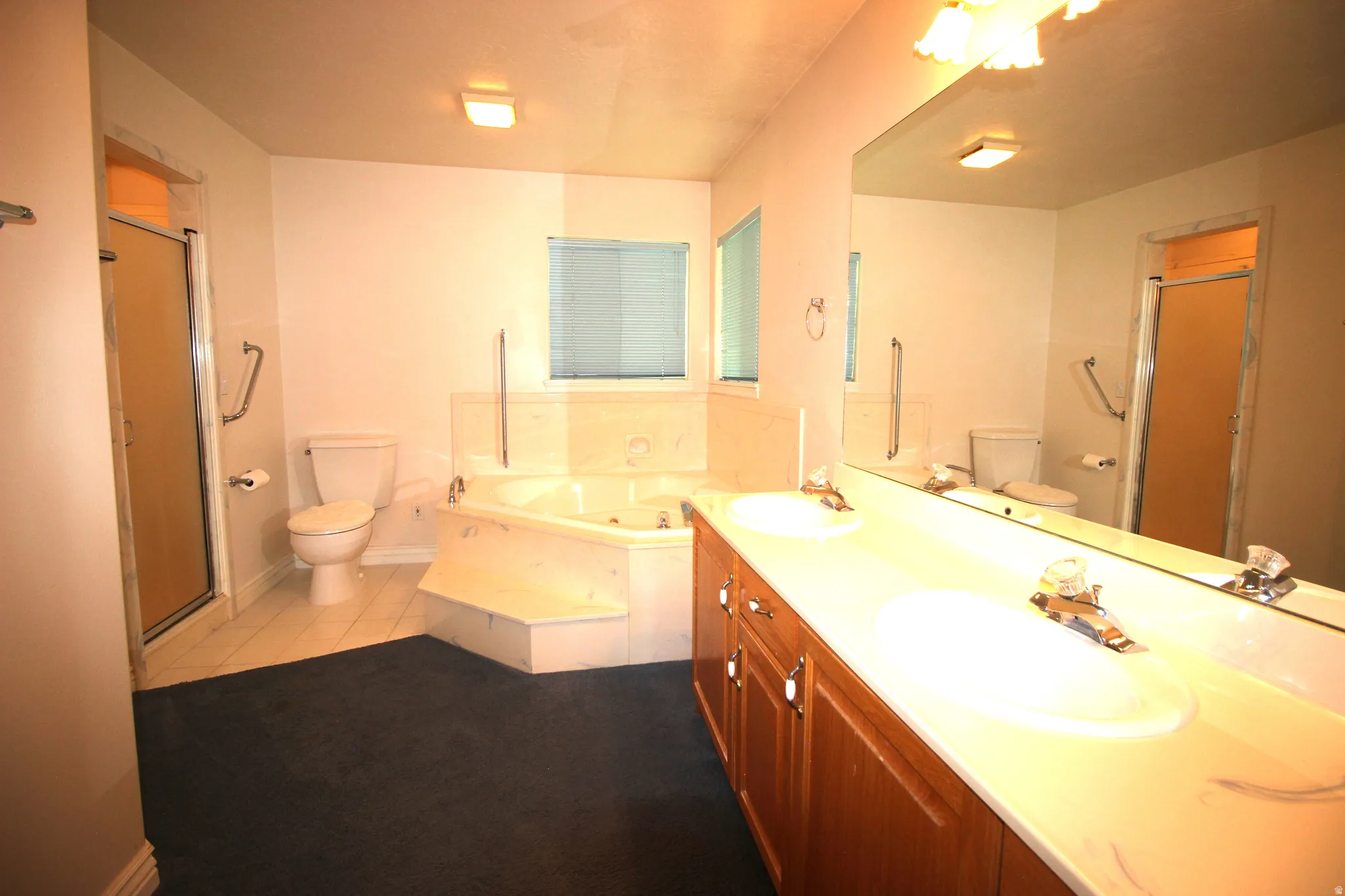 Dual vanity with integrated sinks, large wall-mounted mirror, corner soaking tub, and a glass-enclosed shower