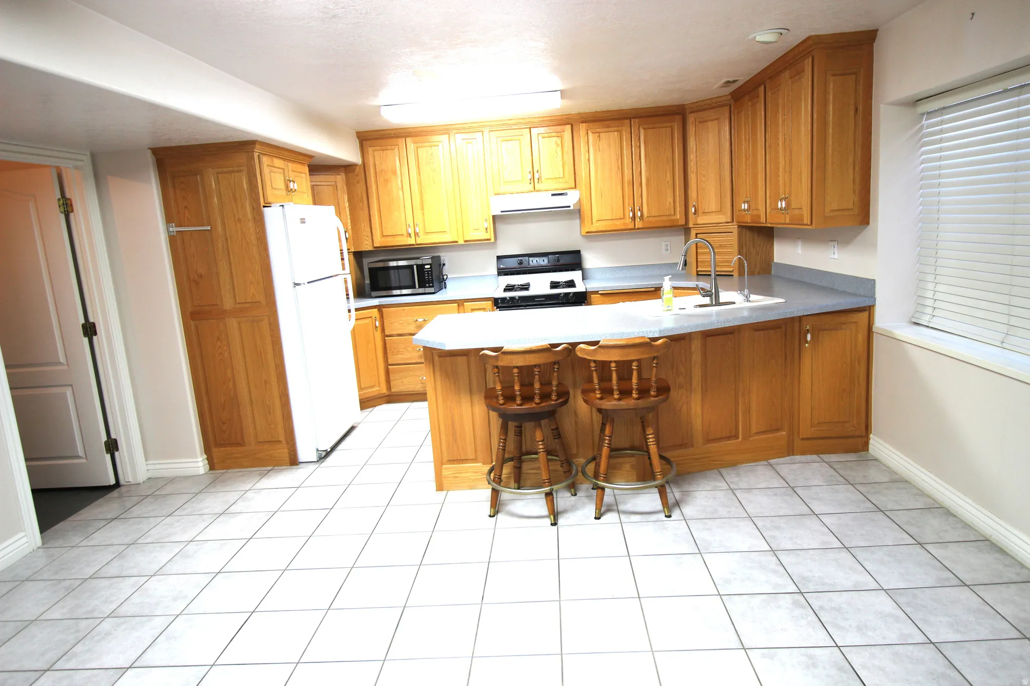 Kitchen featuring light-tone wood cabinetry, light-tone countertops, stainless steel sink with a high-arch faucet, and tile flooring