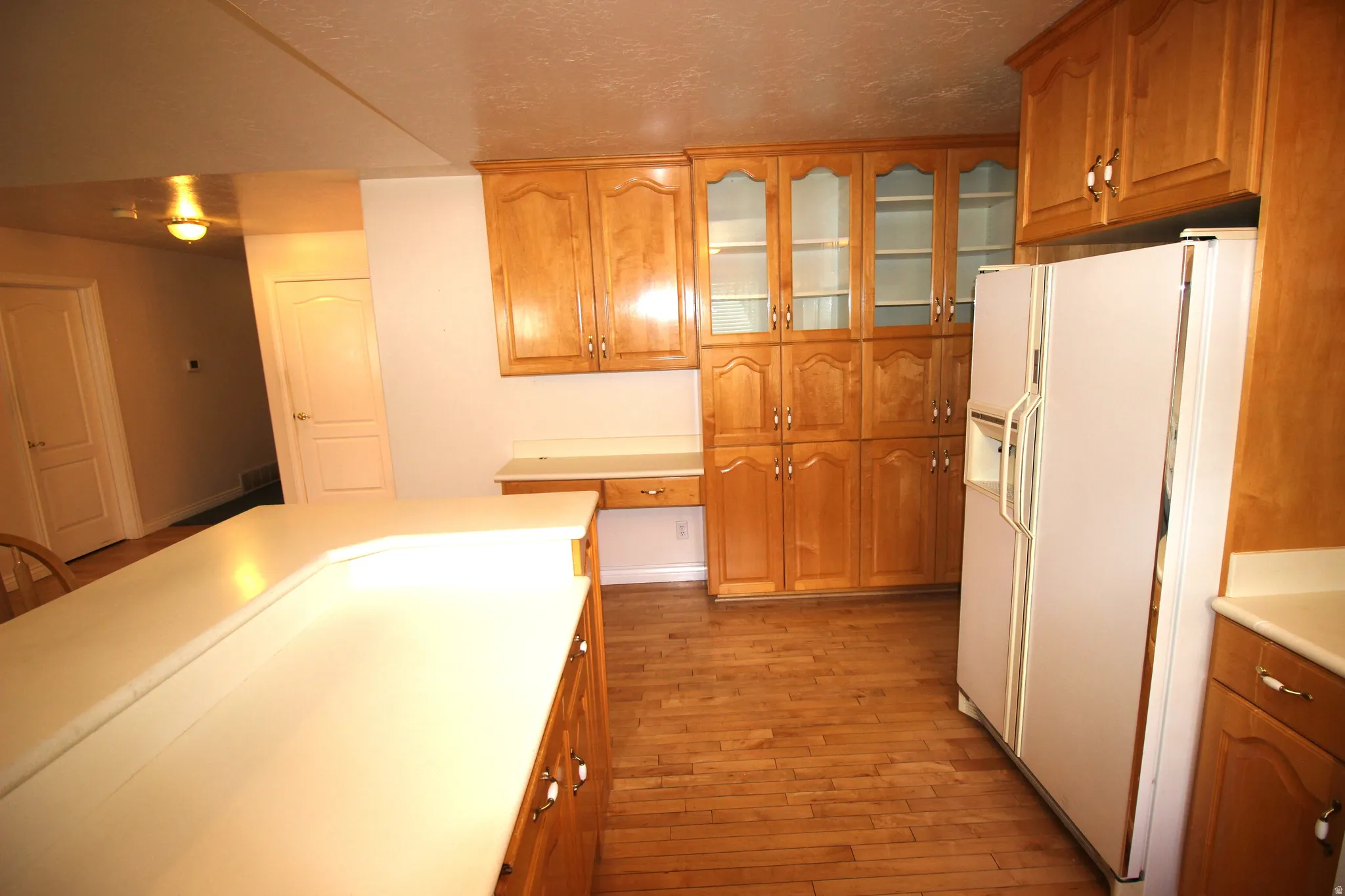 Wood-finish flooring throughout, extensive cabinetry with glass-front uppers, and a refrigerator with a dispenser