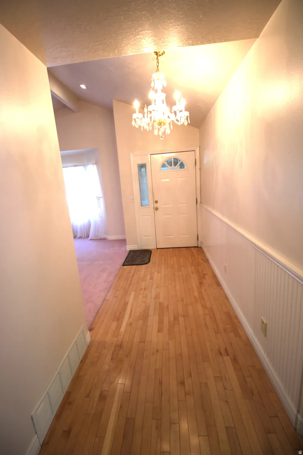Entryway featuring wood flooring, wainscoting, a decorative chandelier, and a front door with an arched transom window