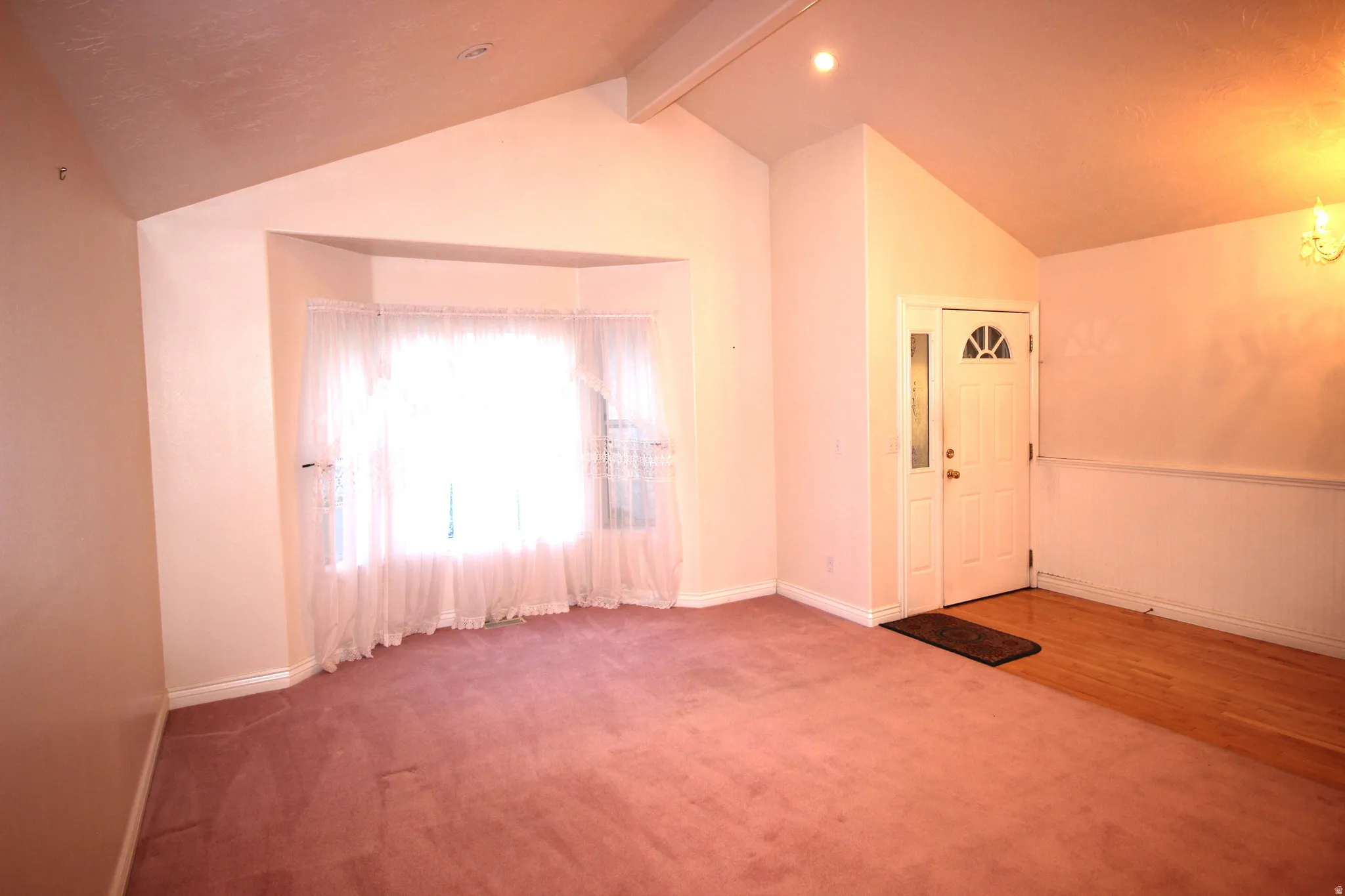 Vaulted ceiling, bay window, recessed lighting, wood-finish flooring, and a paneled entry door with decorative glass