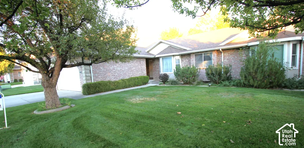 Brick exterior home with a two-car garage, mature front yard trees, and established shrubbery