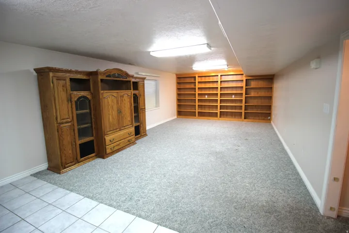 Expansive room featuring wall-to-wall built-in wood shelving, a tiled entry area, and light gray carpeting