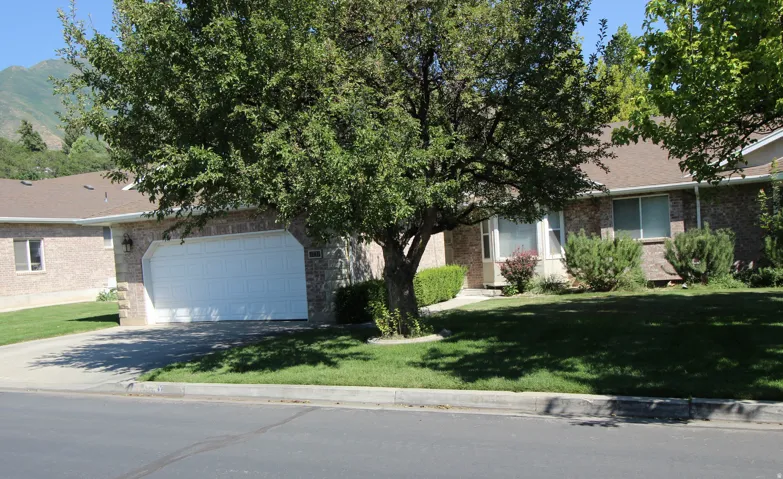 Brick exterior featuring a two-car garage, mature trees, and a mountain backdrop
