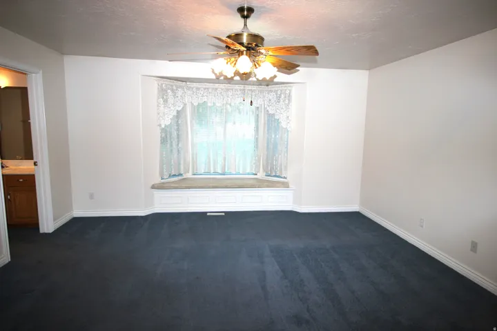 Spacious Master Bedroom with blue carpeting, a bay window with integrated window seat, and a ceiling fan with integrated lighting