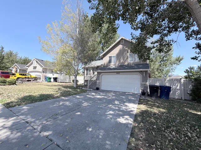 Two-story stucco residence featuring an attached two-car garage, partial stone facade, and a fenced side yard
