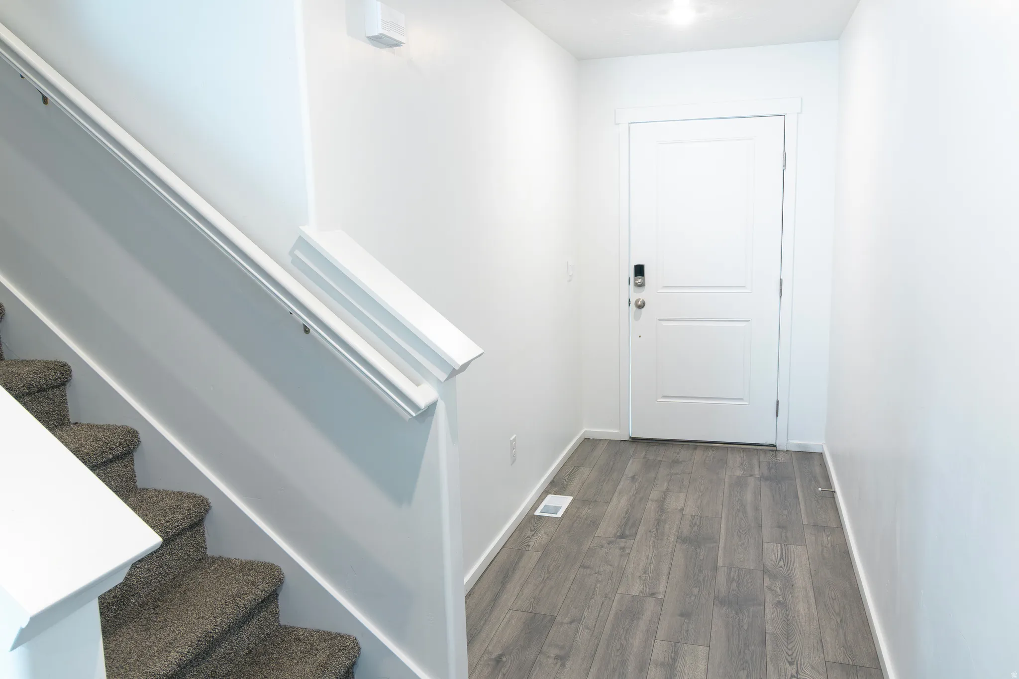 Foyer featuring wood-finish flooring and a white paneled door with contemporary hardware
