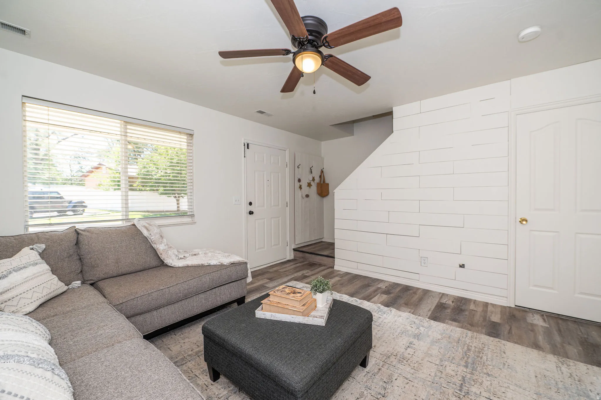 Living room showing large front window, stairs to second level, under stairs closet and shiplap detailing.