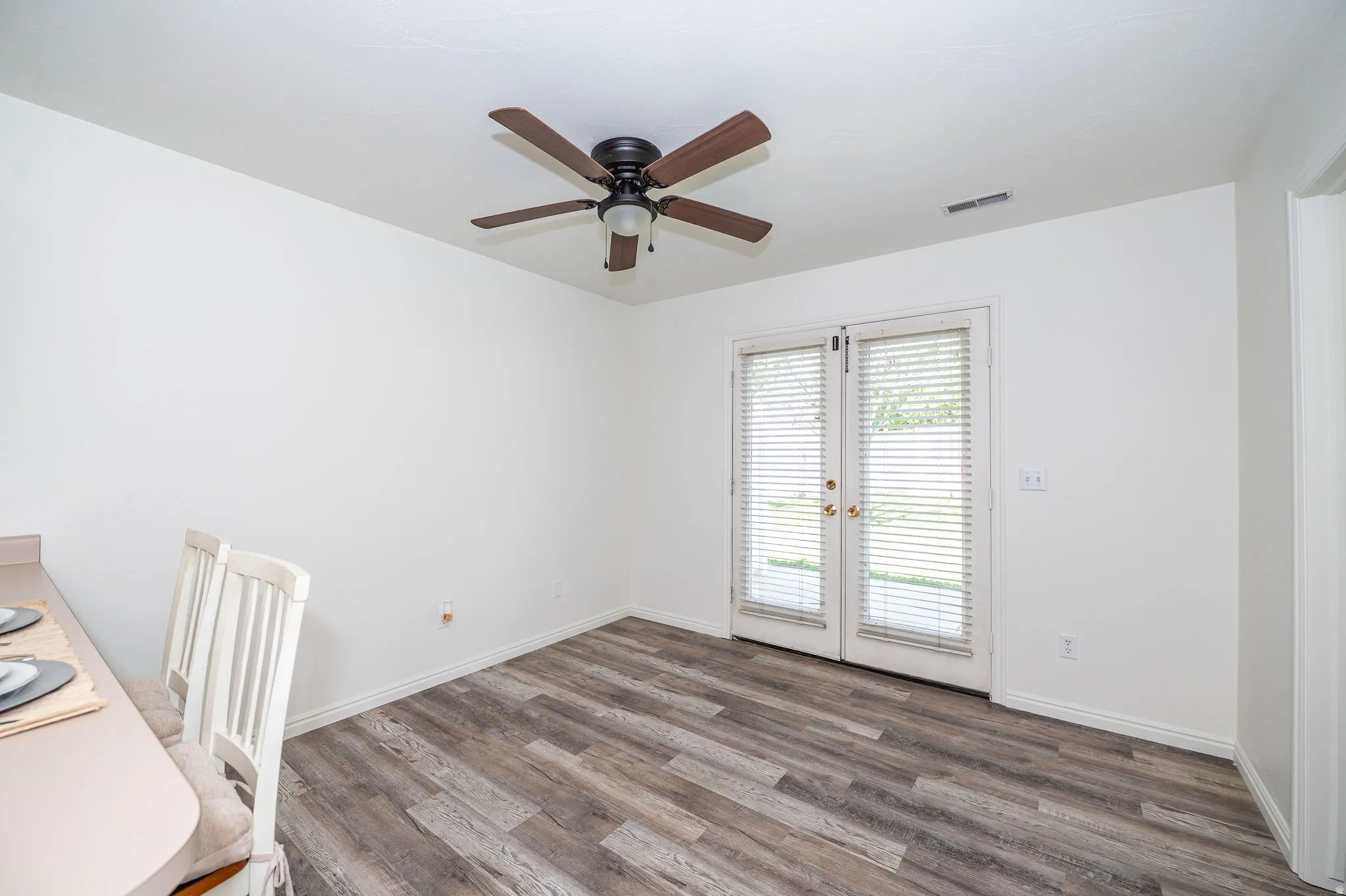 Bright interior dining area featuring LVP flooring, a ceiling fan with integrated lighting, french doors to private patio, and freshly painted walls.