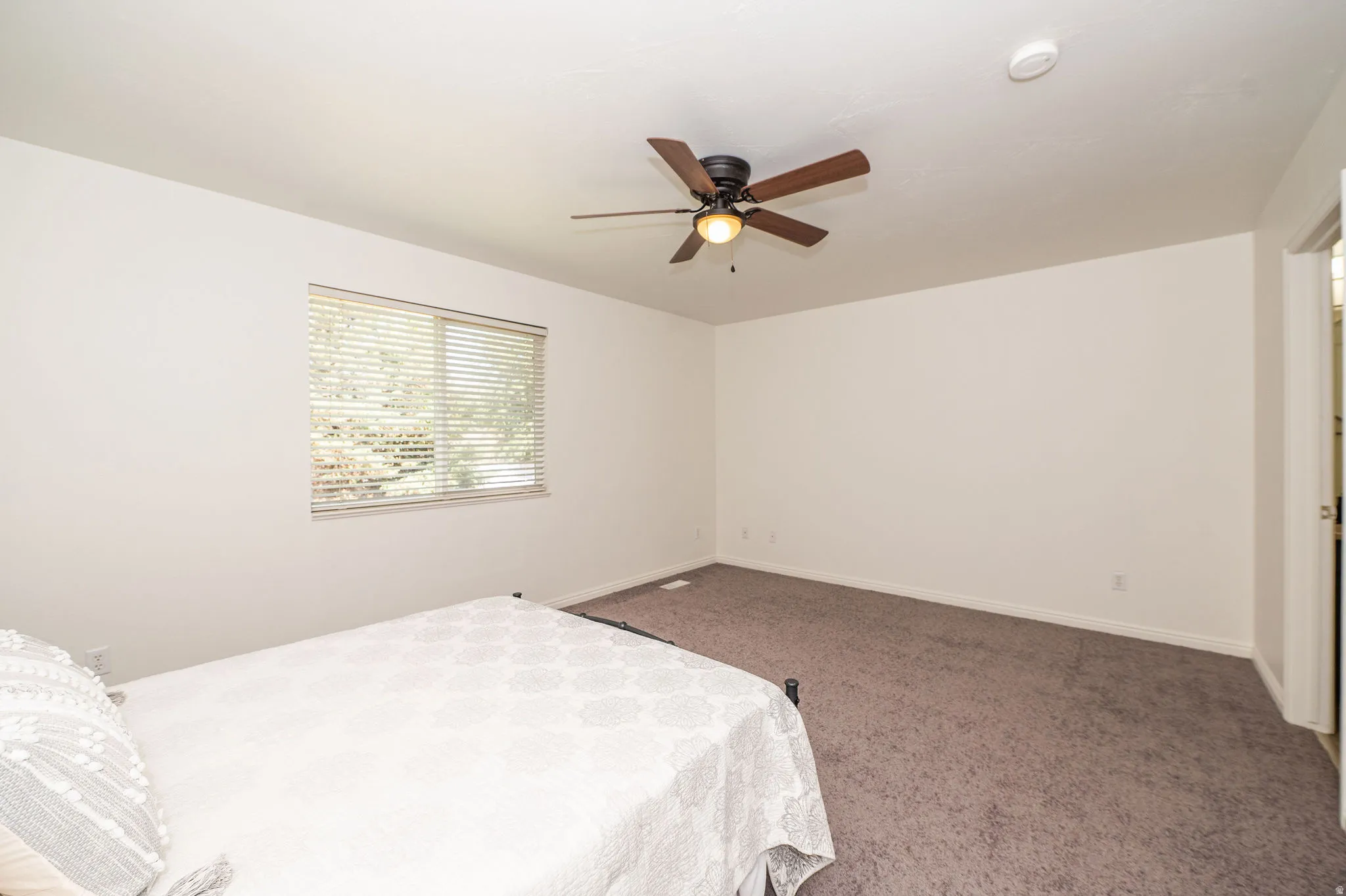 Spacious room with light-colored walls, new carpet, and a ceiling fan with integrated lighting.