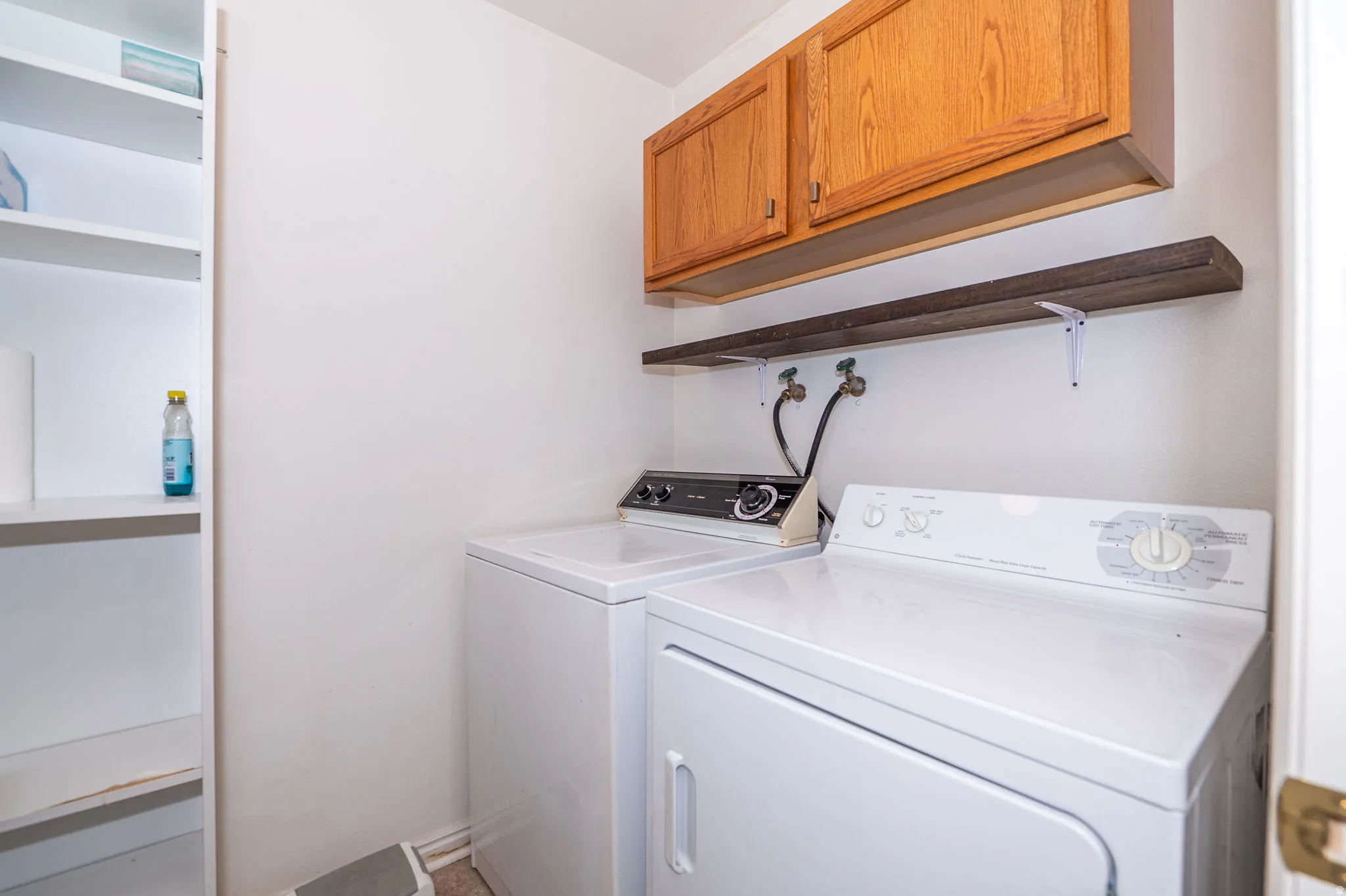 Dedicated laundry area featuring a built-in shelving unit, wood-finish overhead cabinetry, and a wall-mounted shelving. Washer and dryer included.