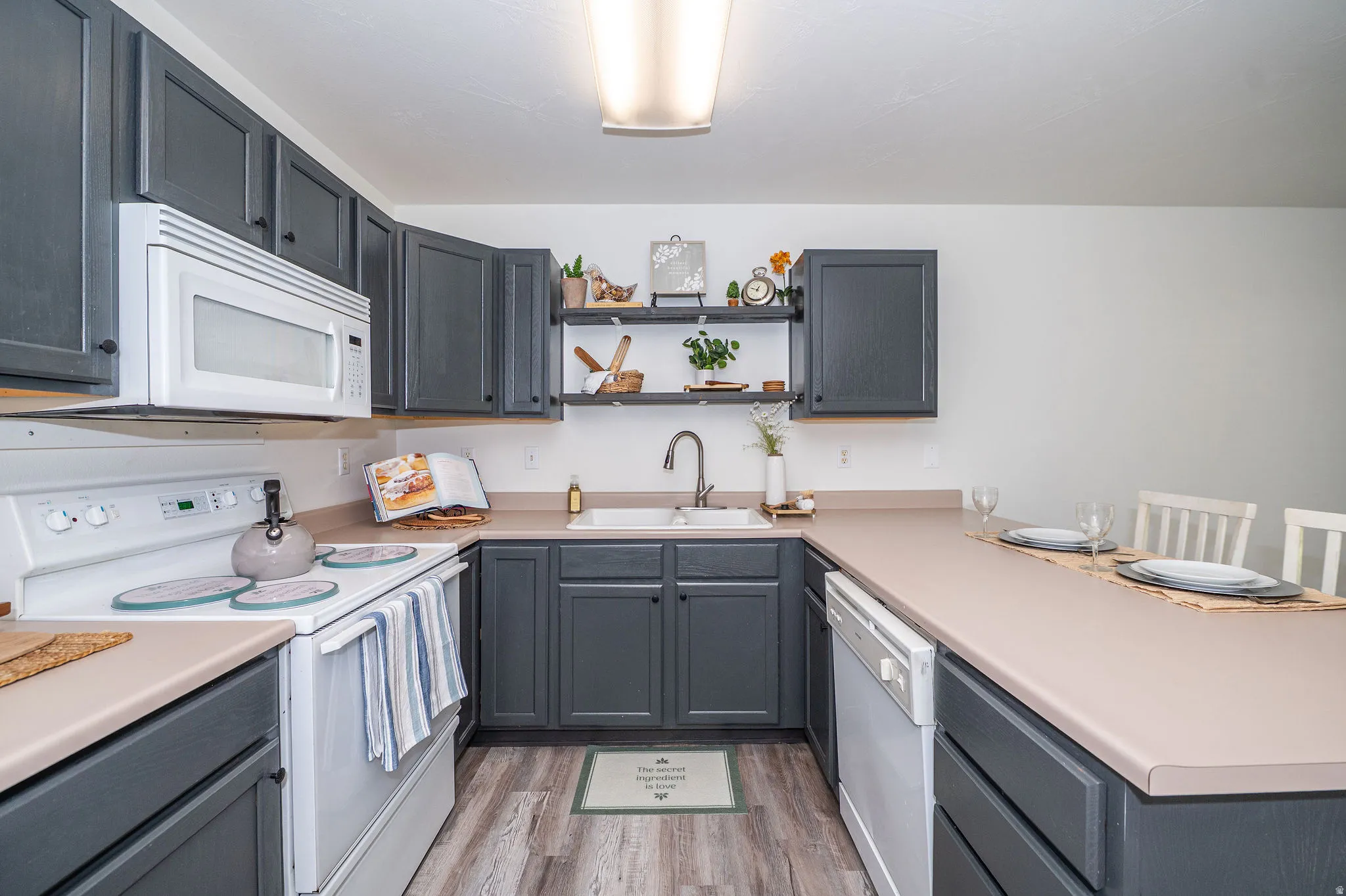 U-shaped kitchen featuring painted cabinetry, formica countertops, built in microwave, and LVP flooring.