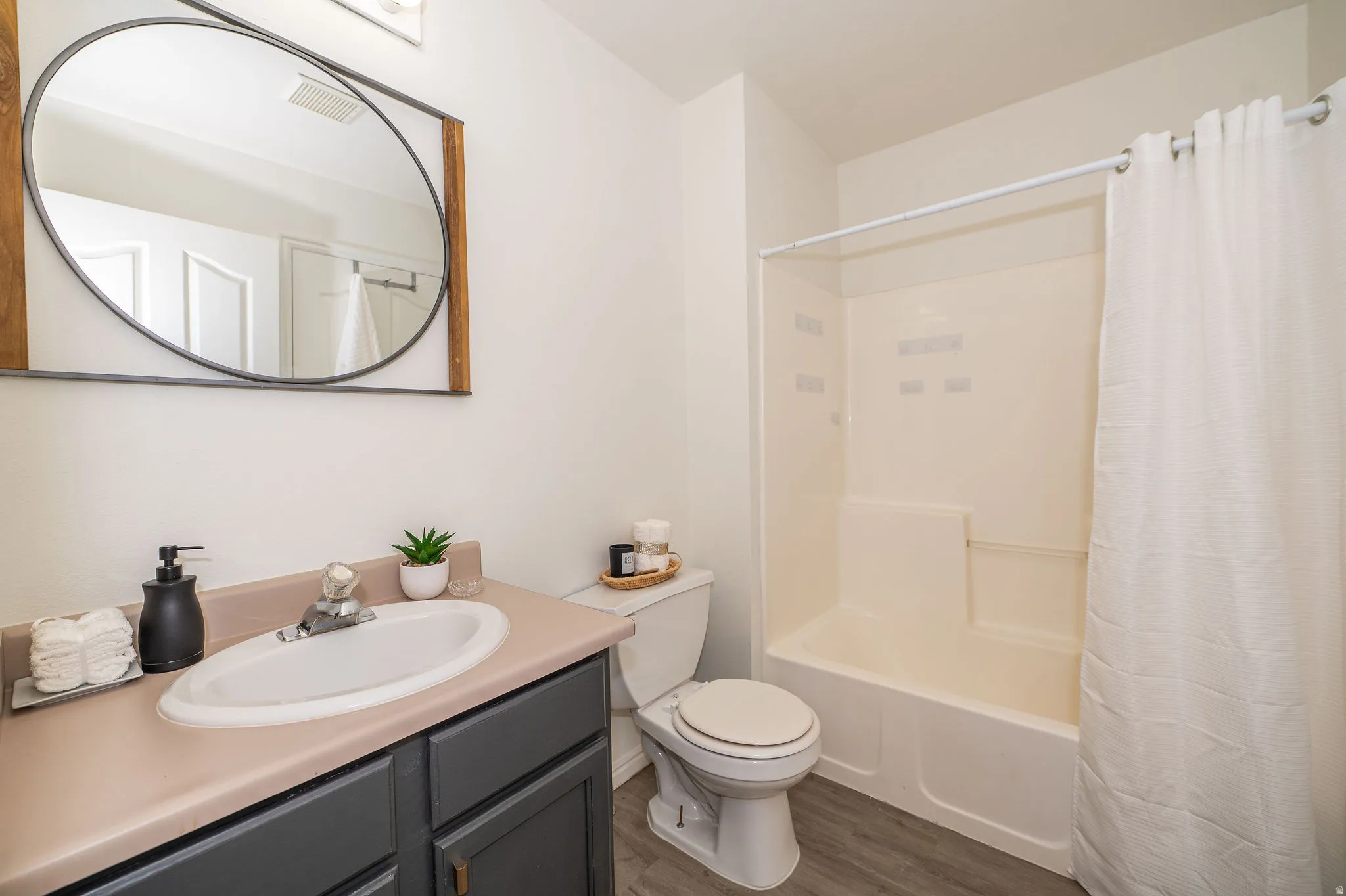 Full bathroom featuring a white bathtub/shower combination, white toilet, and a vanity with a white oval sink set into a light-colored formica countertop.