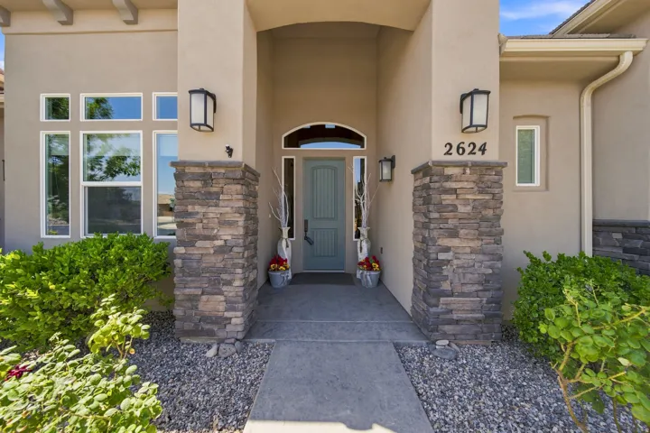 Stucco exterior featuring stacked stone accents, a covered entry, and a light blue paneled door with an arched transom window
