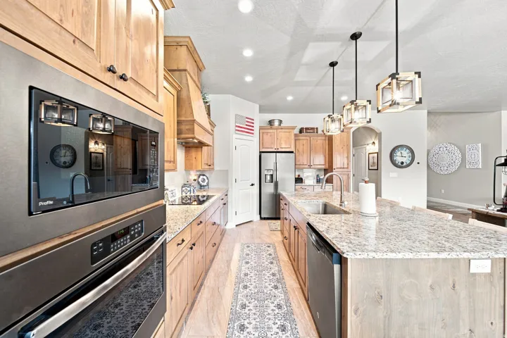 Kitchen featuring light wood cabinetry, a built-in oven and microwave, stainless steel appliances, a large island with an undermount sink, and recessed lighting
