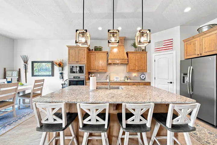Spacious kitchen featuring a large island with seating, pendant lighting, stainless steel appliances, light wood-finish cabinetry, and solid surface countertops