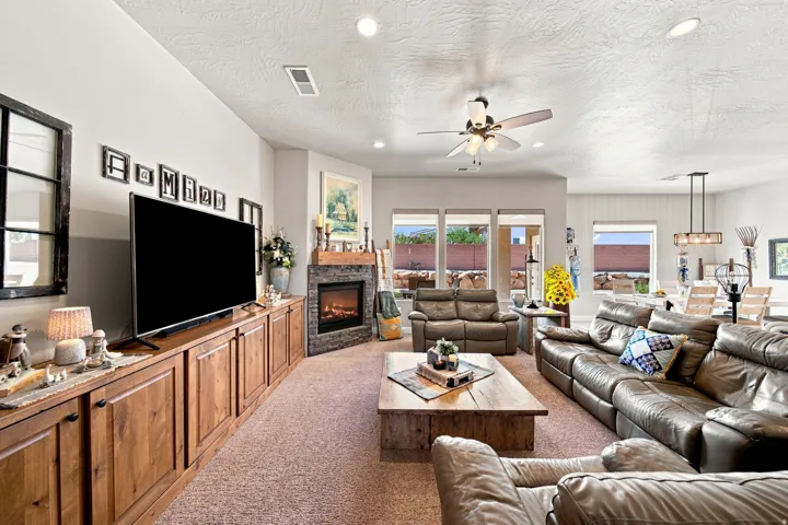Expansive living area featuring a stone-clad corner fireplace with wood mantle, built-in wood cabinetry, and multiple large windows