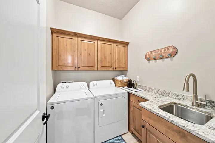 Dedicated laundry space featuring upper wood cabinetry, a granite-finish countertop, and an undermount stainless steel sink with a gooseneck faucet