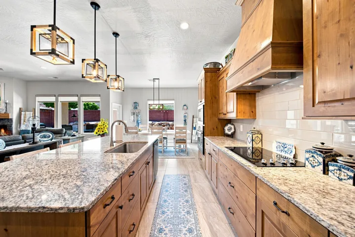 Gourmet kitchen featuring a large island with sink, granite countertops, wood-finish cabinetry, built-in cooktop, and subway tile backsplash