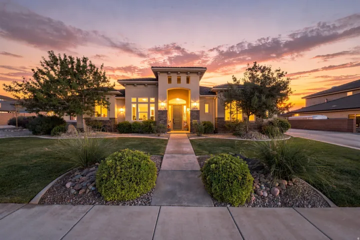 Sleek contemporary residence featuring a stucco and stone exterior, a concrete walkway, mature landscaping with shrubs and trees, and a manicured lawn